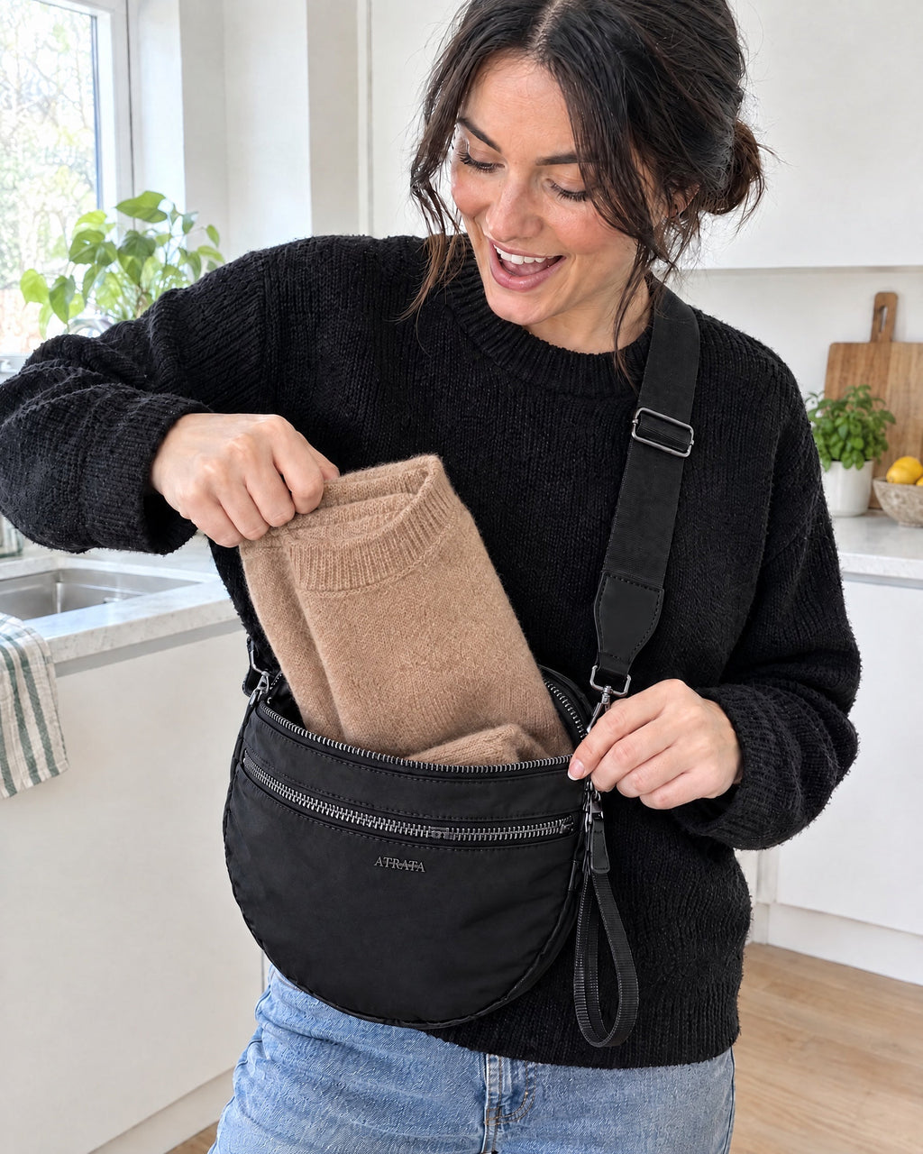 The Kelaino Crossbody, a folded jumper being taken out of the bag